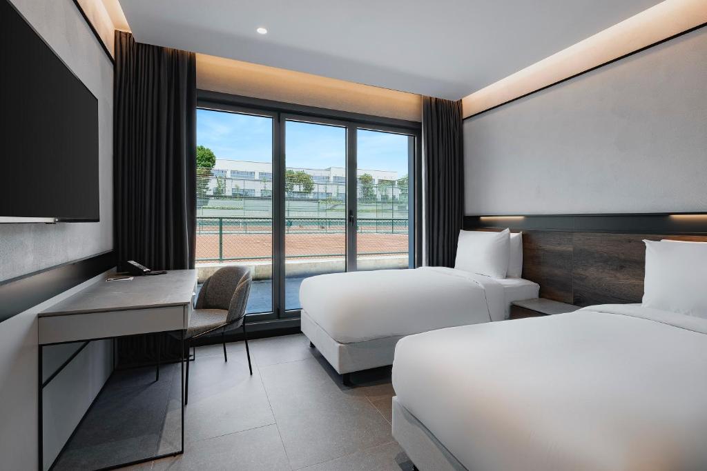Zweibettzimmer mit Balkonblick auf die Tennisplätze, ausgestattet mit Schreibtisch und minimalistischem Design.