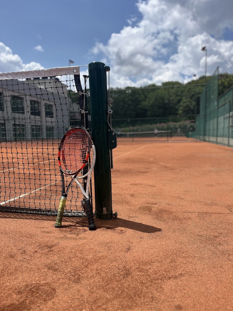 Tennisnetz auf einem Sandplatz mit zwei Schlägern am Pfosten.