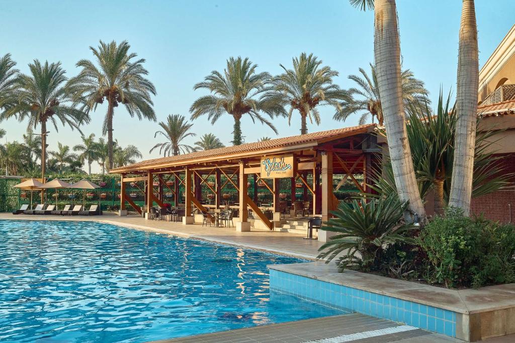 Outdoor swimming pool with a poolside bar pavilion, sun loungers, and palm trees.
