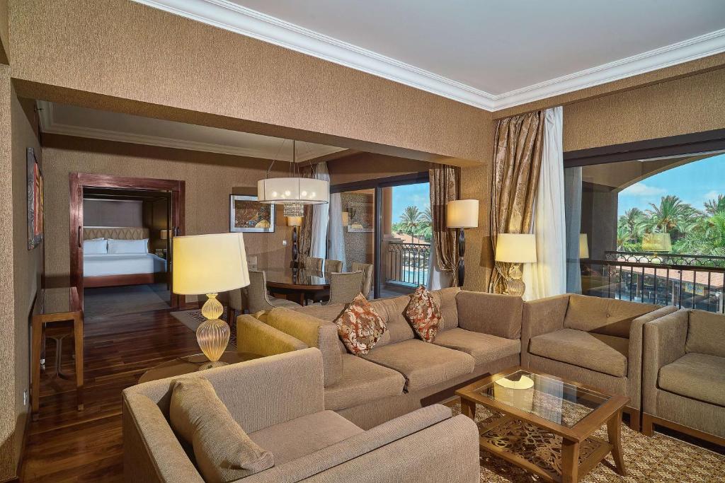 Hotel suite living area with sofas, coffee table, dining space, and balcony doors.