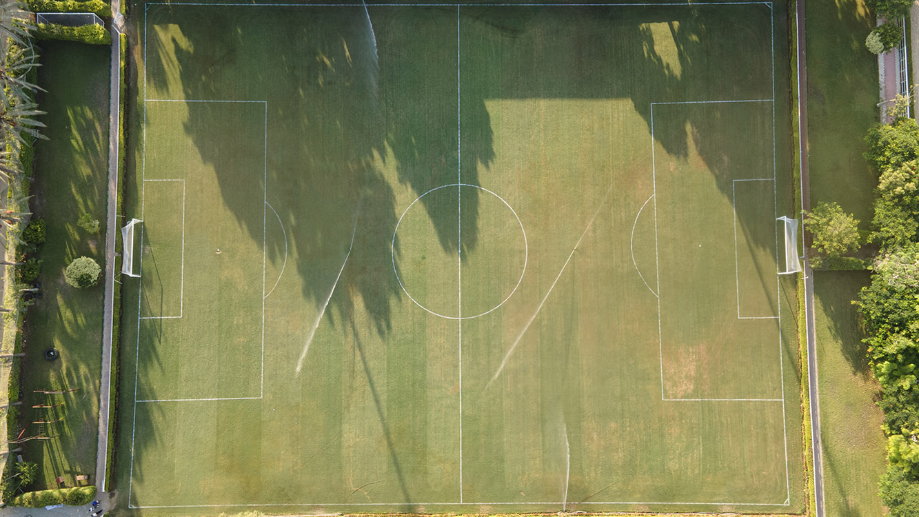 Aerial view of a full-size football pitch with goals and sprinklers on the turf.