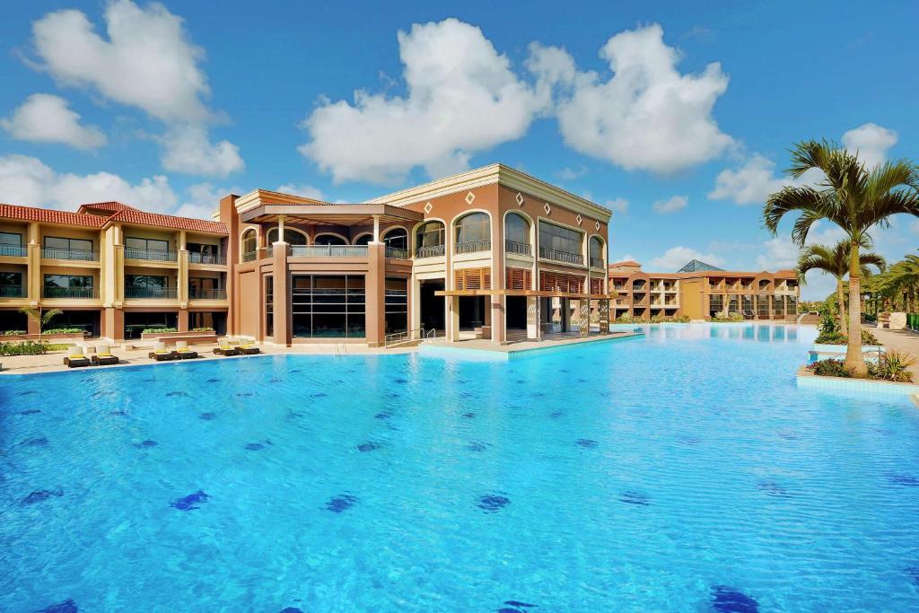 Large resort swimming pool in front of the hotel buildings under a blue sky.