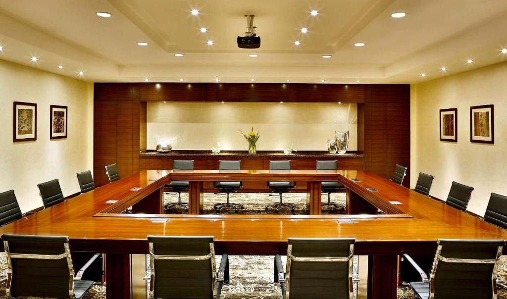 Boardroom-style meeting room with U-shaped conference table, chairs, and ceiling projector.