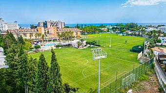 Aerial view of resort area with two football pitches and surrounding buildings near the coast.