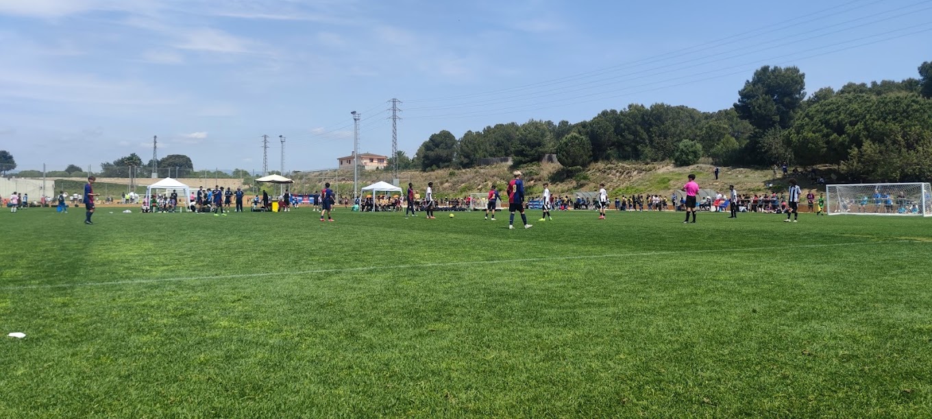 Weitwinkelansicht eines Fußballspiels auf Rasen mit Zelten an der Seitenlinie und Zuschauern.