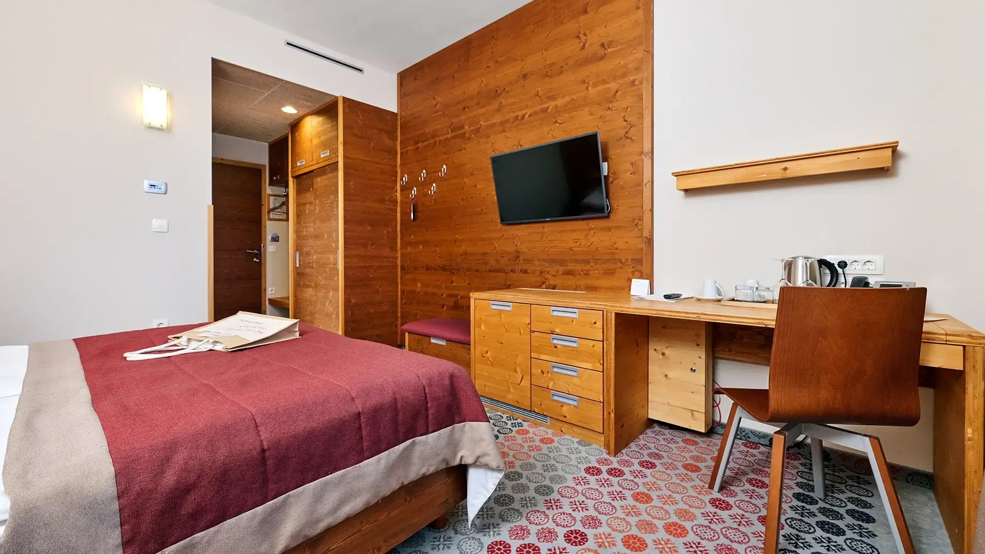 Guest room with wooden desk, wall-mounted TV and storage units.