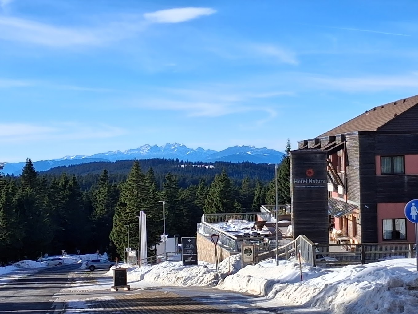 Snowy hotel exterior with mountain views and a forested road approach.