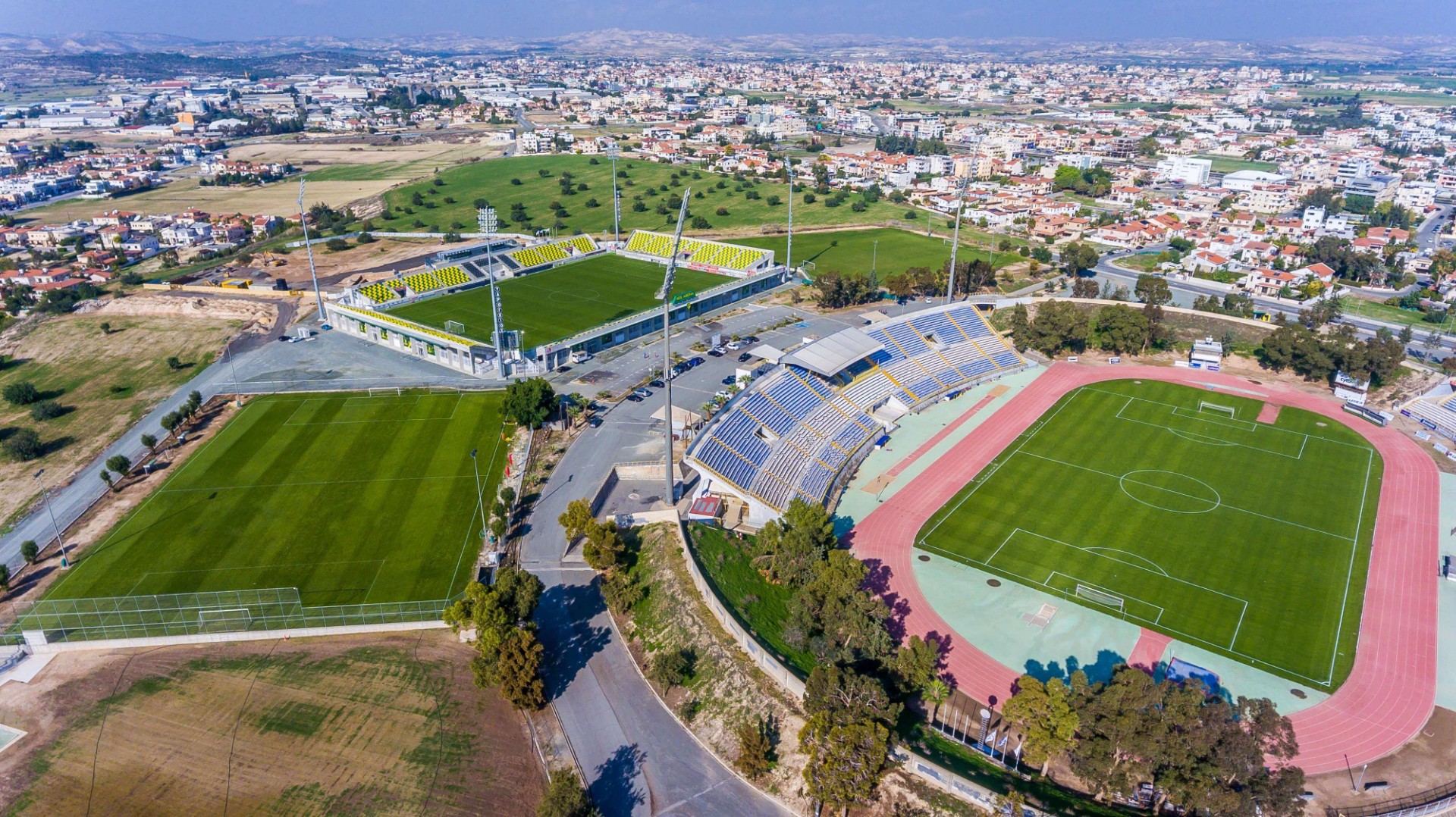 Luftaufnahme von Stadion, Spielfeldern und Sportgebäuden an der Straße.