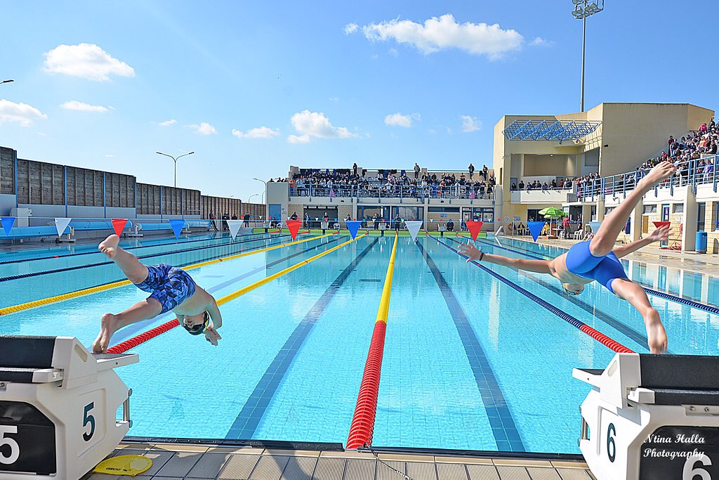 Schwimmer springen von Startblöcken in ein Outdoor-Wettkampfbecken.
