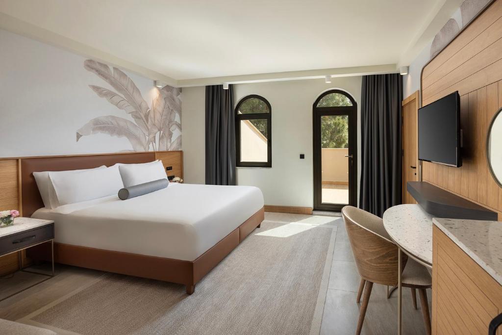 Modernes Zimmer mit Kingsize-Bett, Schreibtisch, Wand-TV und Balkontür mit Rundbogenfenstern.