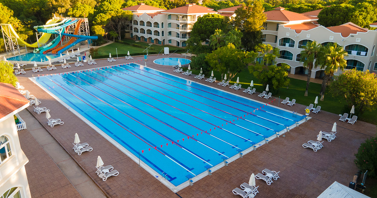 Großer Außen-Trainingspool mit Schwimmbahnen, Sonnenliegen und bunten Wasserrutschen in der Nähe.