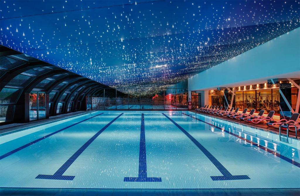 Innenpool mit markierten Schwimmbahnen, Liegestühlen und einer Decke voller sternähnlicher Lichter.