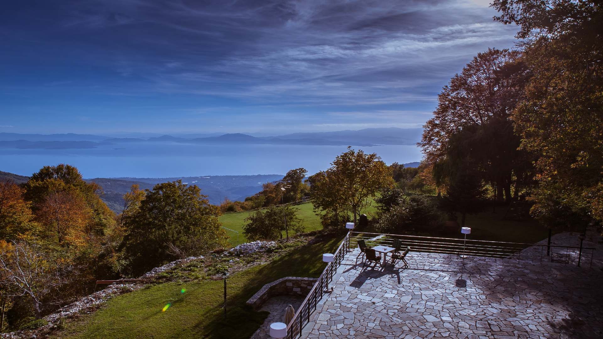 Stone terrace with outdoor seating and panoramic lake and mountain views.
