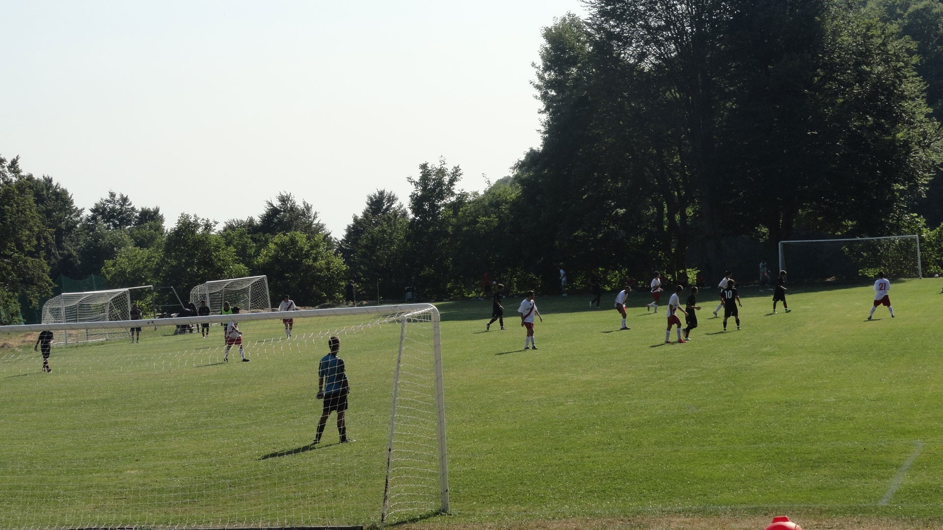 Players on a football pitch with multiple goals and trees around the field.