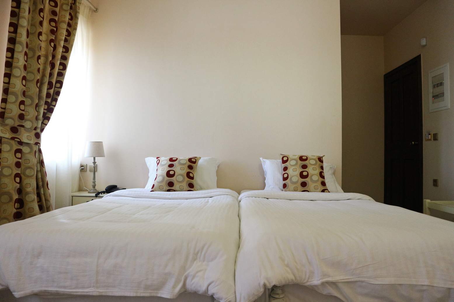 Twin room with two beds, patterned cushions and a bright window.