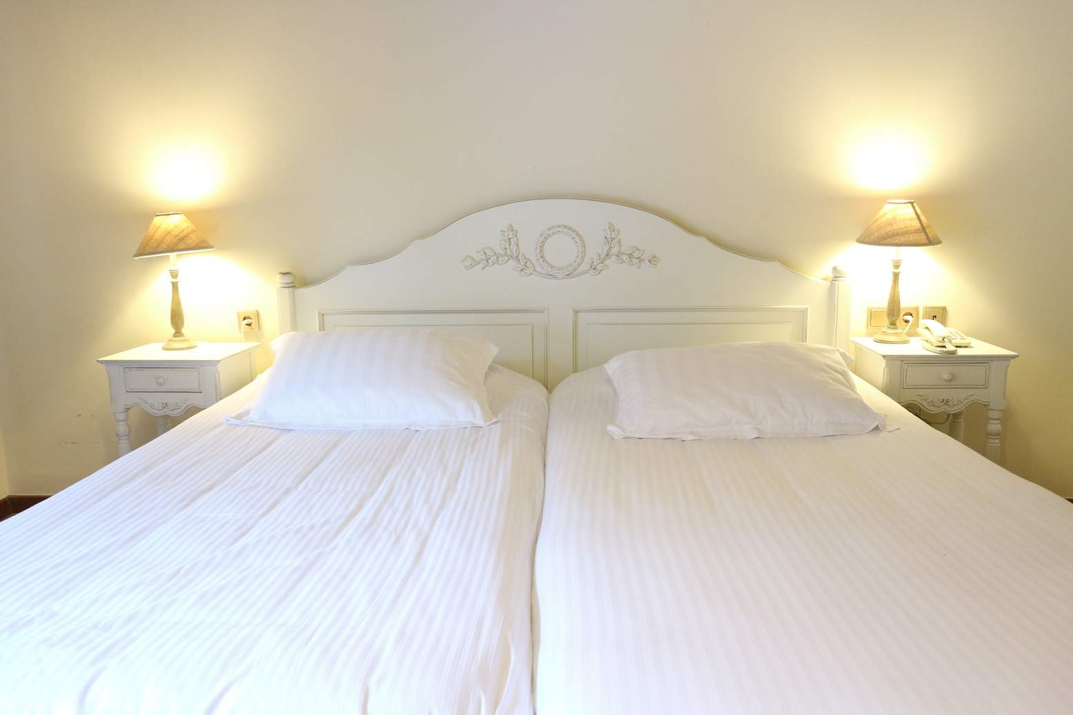 Twin beds with white headboard, bedside tables and lamps.