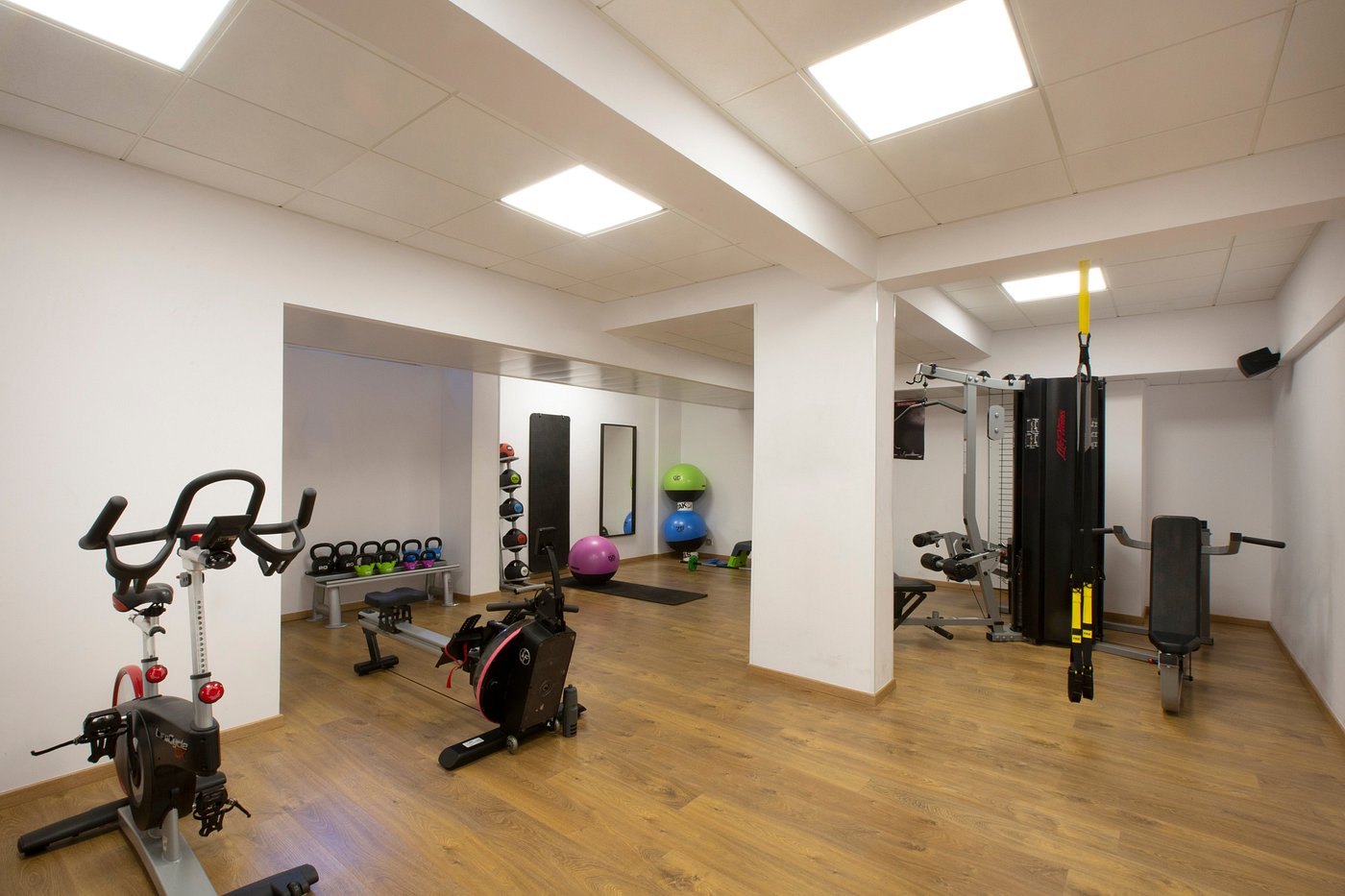 Hotel gym with exercise bikes, weights, and workout equipment on wooden flooring