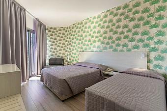 Hotel room with two double beds, green patterned wallpaper, and armchair