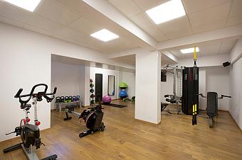 Hotel gym with exercise bikes, weights, and workout equipment on wooden flooring