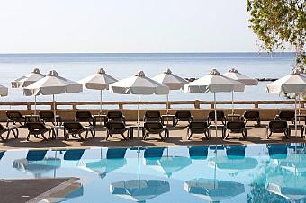 Poolside view with rows of sun loungers and white umbrellas overlooking calm blue sea