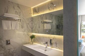 Elegant marble bathroom with illuminated mirror, white sink, and neatly folded towels on racks