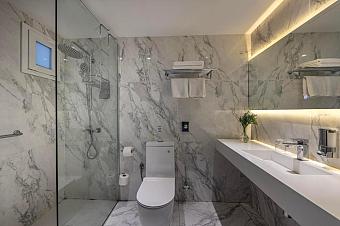 Spacious marble bathroom with glass shower, toilet, long countertop, and ambient lighting