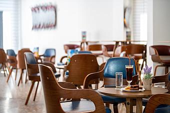 Modern hotel café with wooden chairs, small tables, and a drink served with snacks and flowers