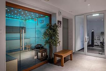 Spa area with glass sauna featuring blue LED lights, wooden bench, and nearby gym equipment