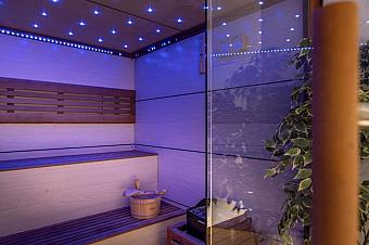 Modern sauna interior with wooden benches, bucket, and soft blue lighting