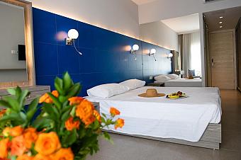 Bright hotel room with double bed, blue accent wall, and bouquet of orange flowers