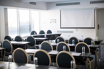 Conference room with rows of chairs and tables facing a projection screen, prepared for a coaching or team meeting