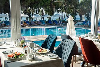 Restaurant dining tables set beside large windows overlooking the pool and sunbeds