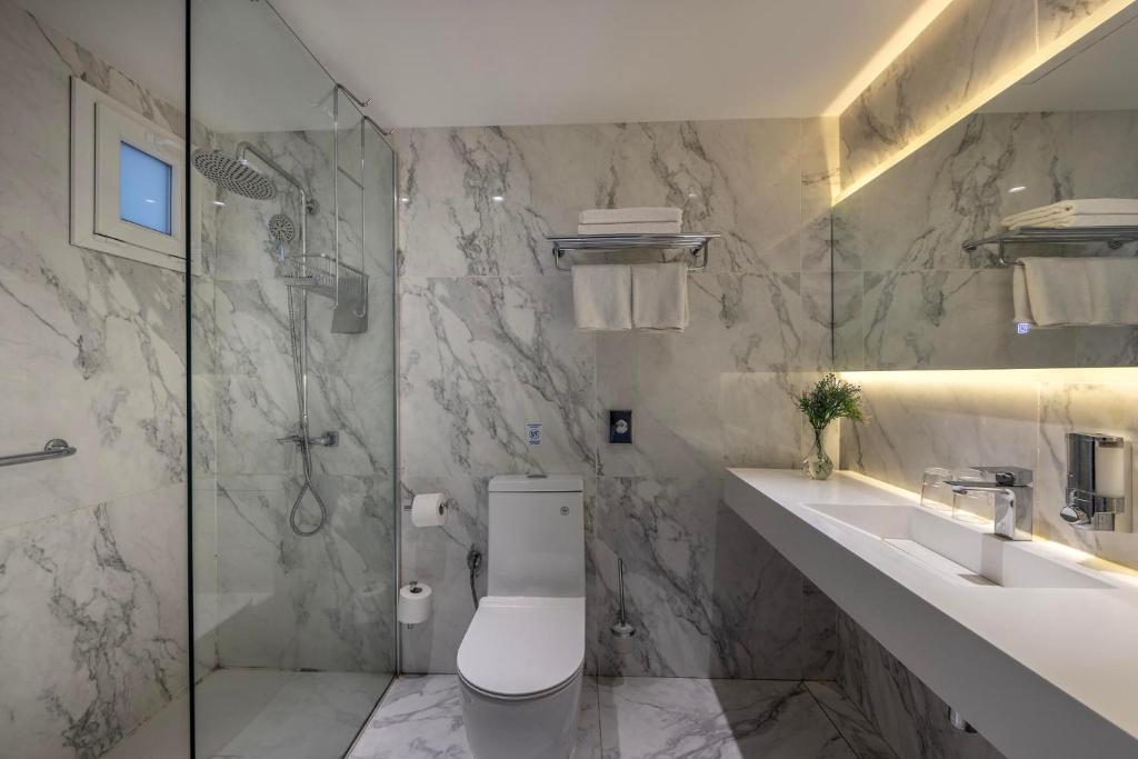 Spacious marble bathroom with glass shower, toilet, long countertop, and ambient lighting