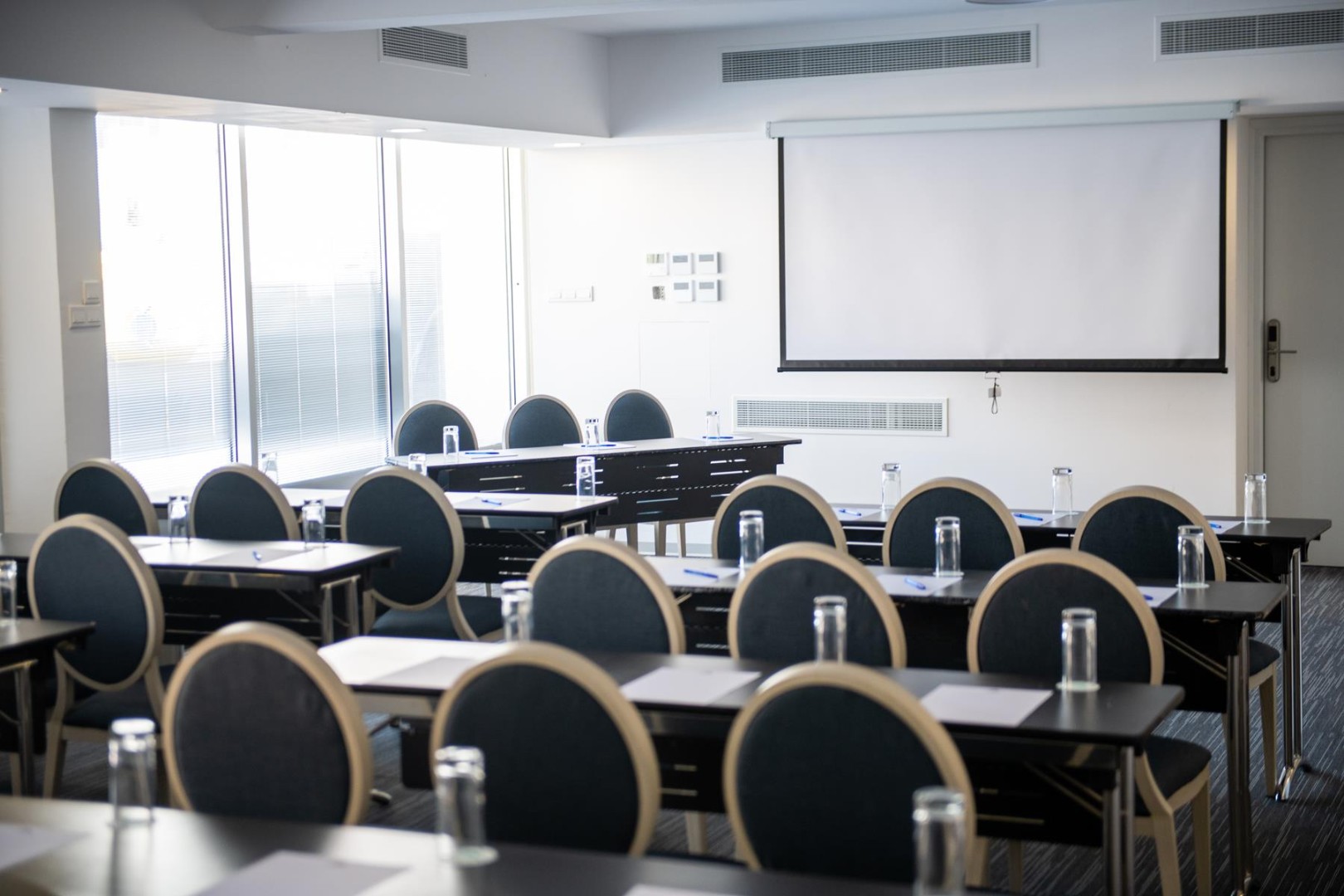 Conference room with rows of chairs and tables facing a projection screen, prepared for a coaching or team meeting