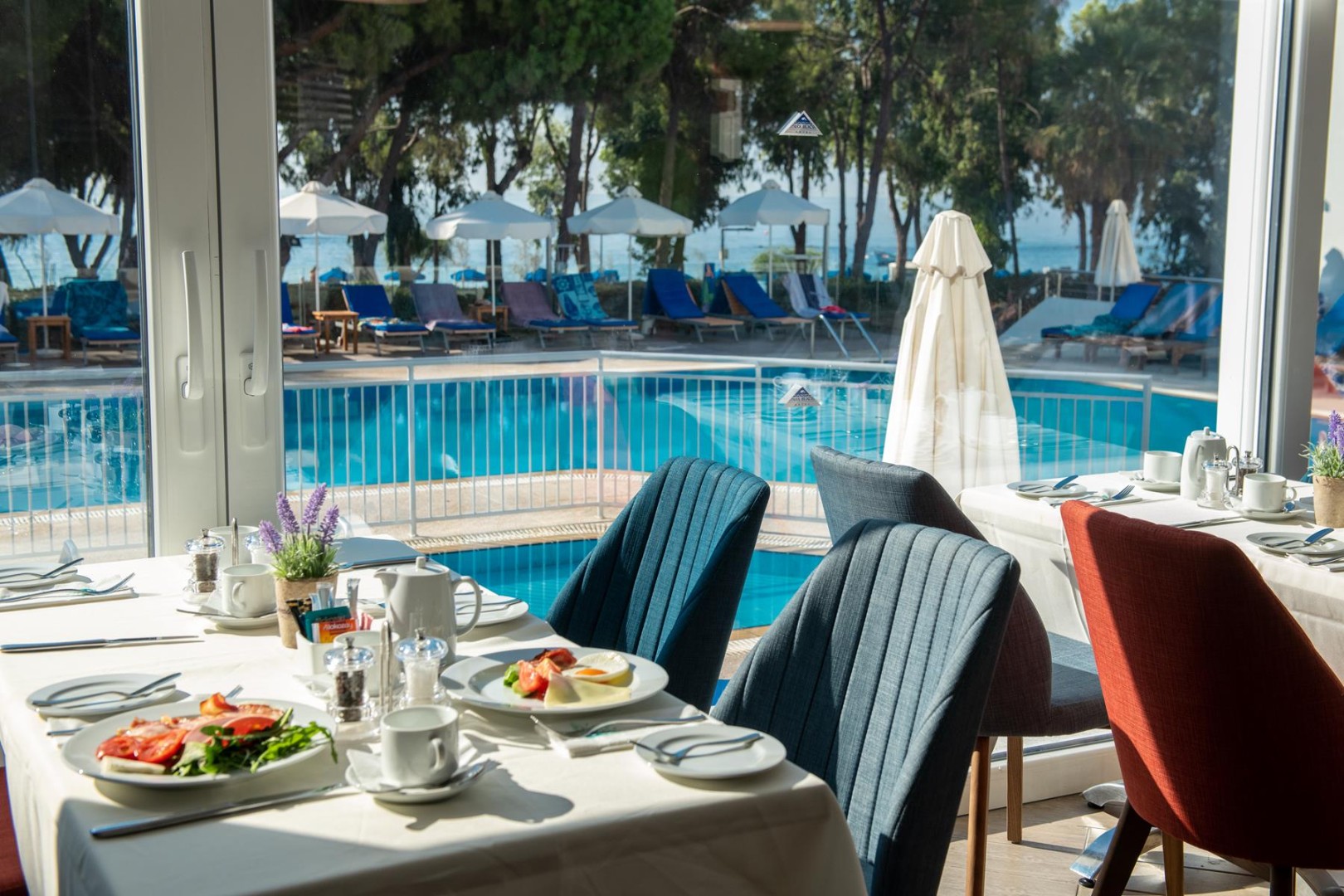 Restaurant dining tables set beside large windows overlooking the pool and sunbeds