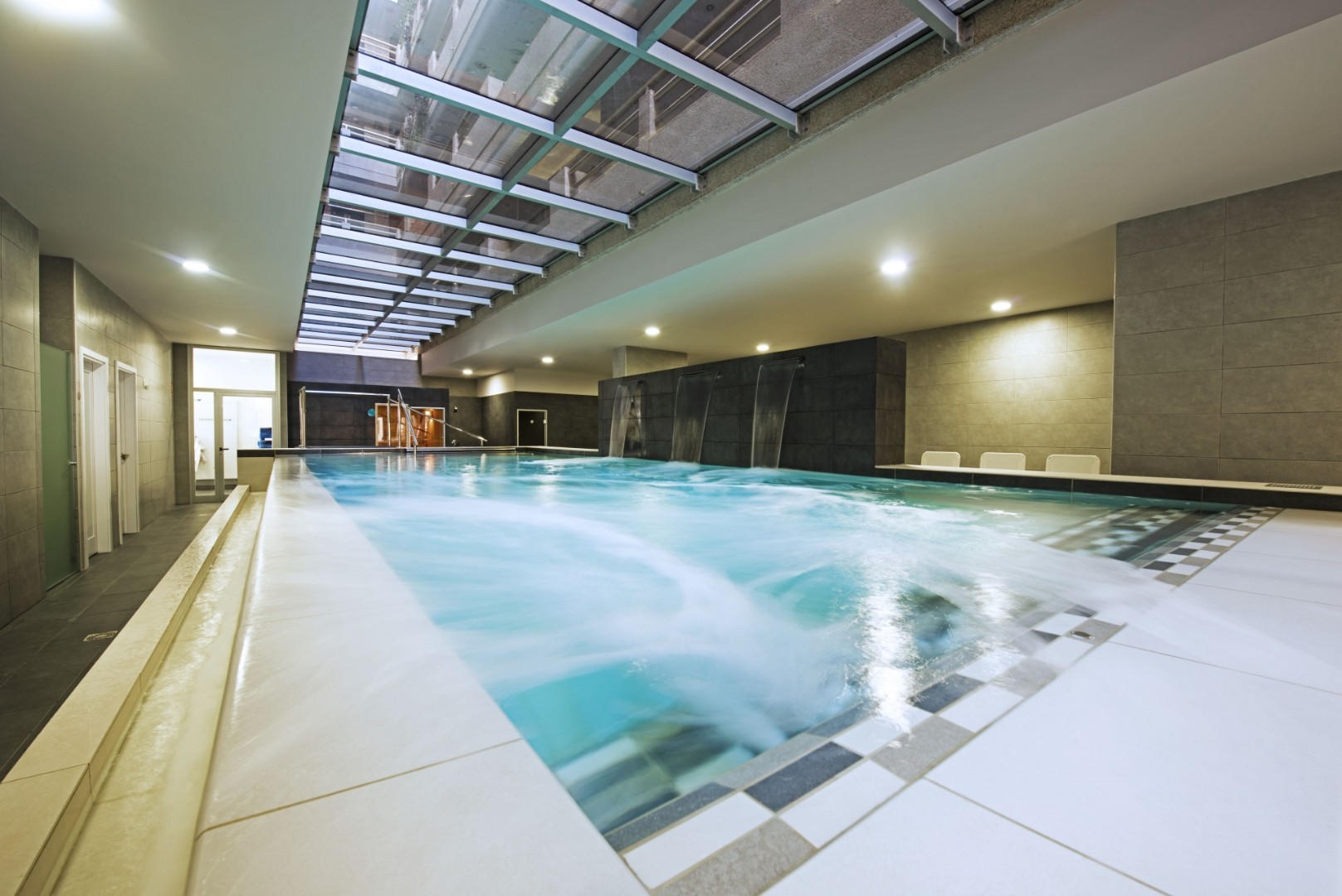 Indoor spa pool with bubbling water, loungers, and skylight ceiling.