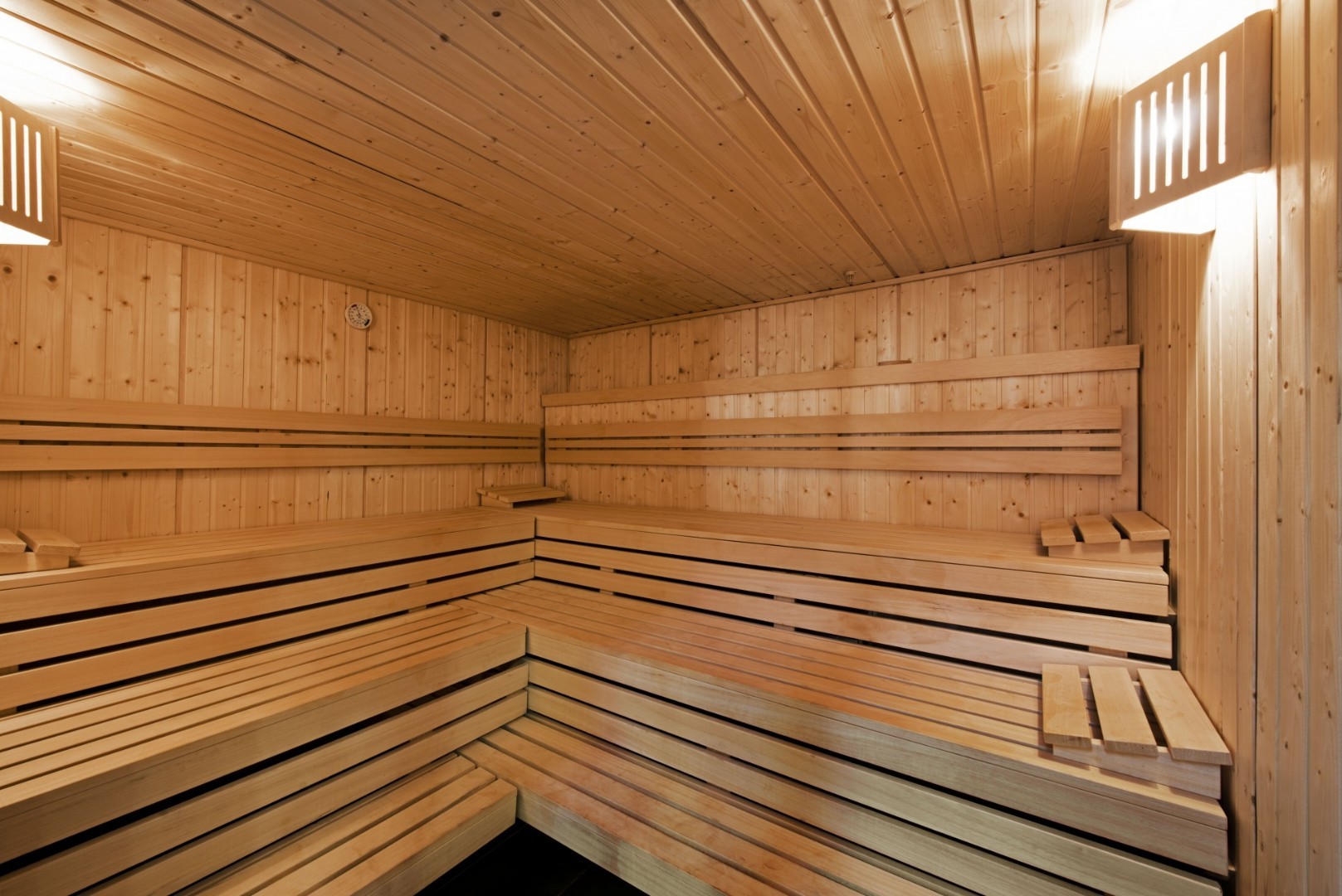 Wood-paneled sauna with tiered benches and wall lights.