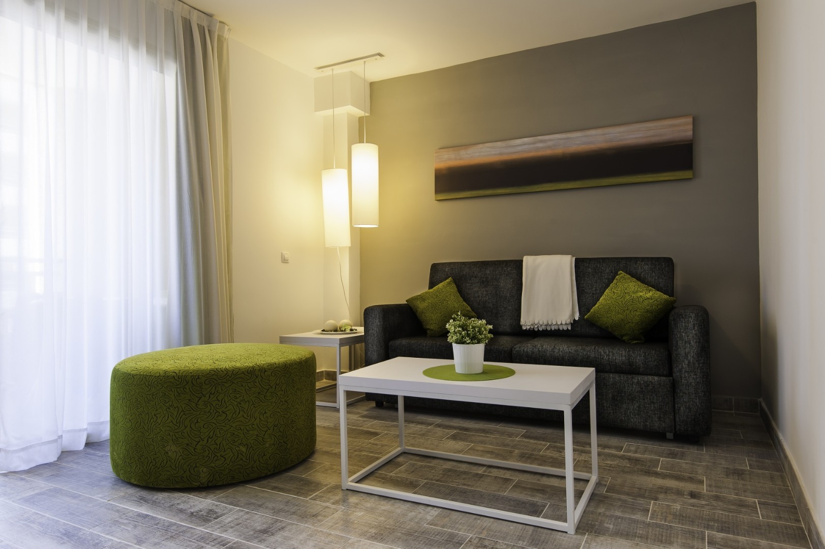 Cozy lounge with gray sofa, coffee table, pendant lights, and a green ottoman.