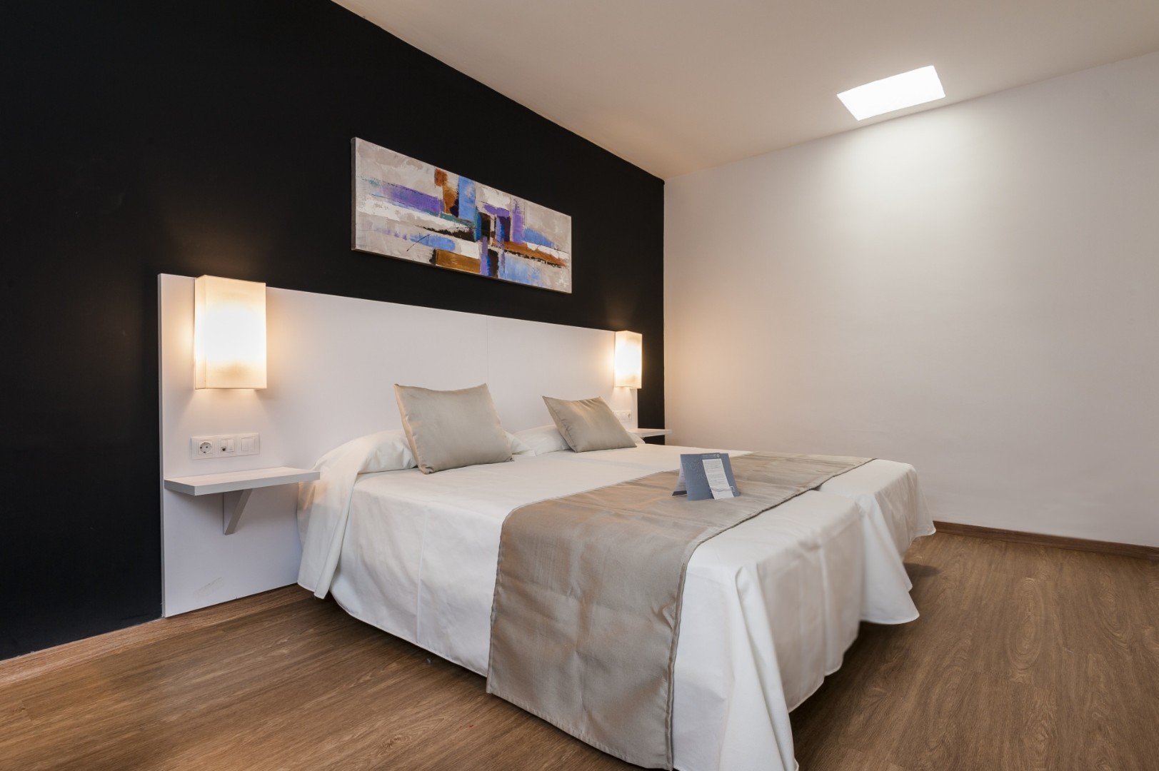 Modern double room with black accent wall, bedside lighting, and a neutral bed runner.