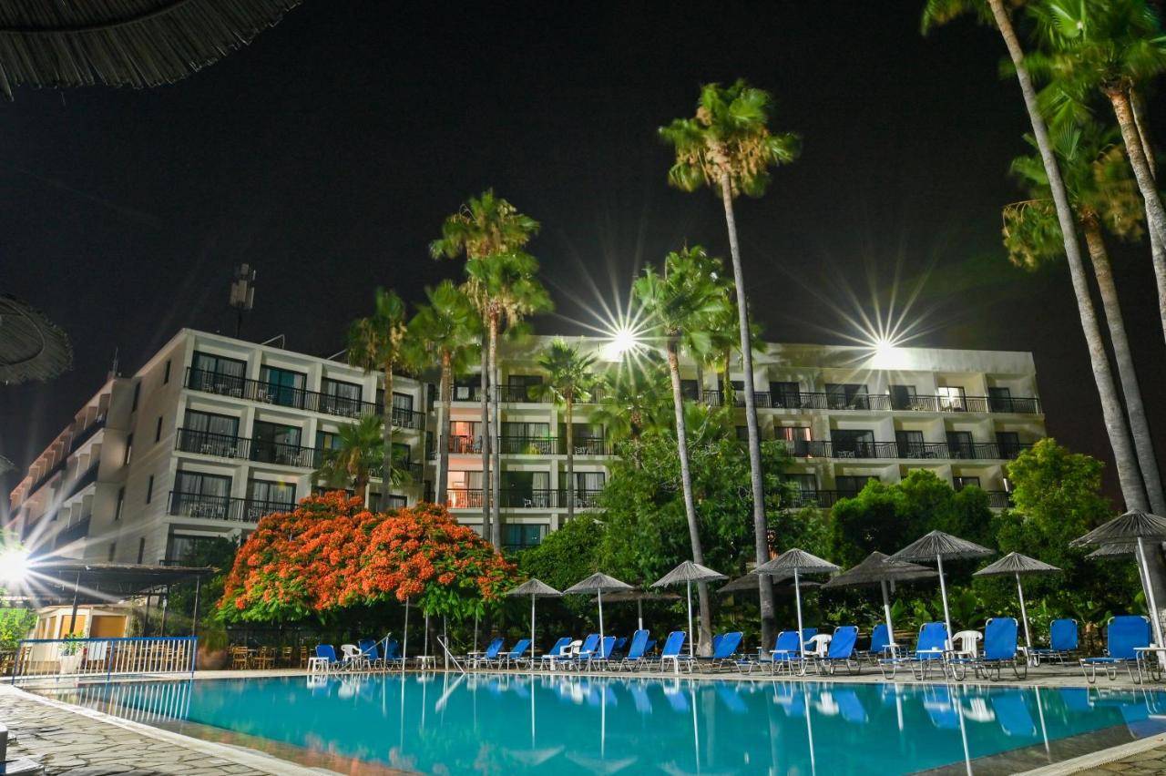 Night view of the hotel exterior and outdoor pool with loungers and palm trees.