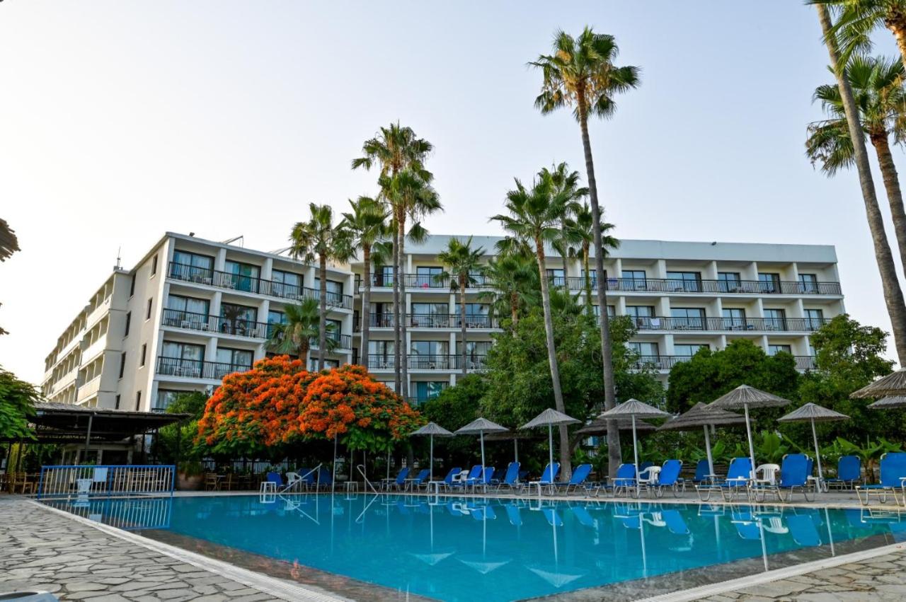 Daytime view of the hotel exterior and outdoor pool with loungers and palm trees.