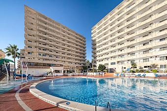 Outdoor pool with surrounding sun deck and multi-storey buildings.