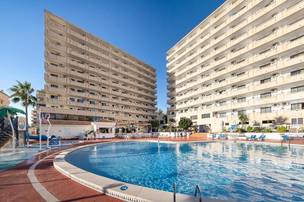 Outdoor pool with surrounding sun deck and multi-storey buildings.
