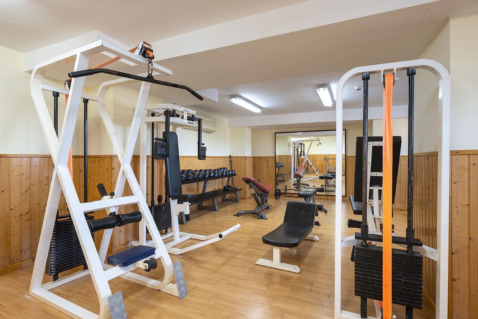 Strength training room with cable machines, benches and a long dumbbell rack.