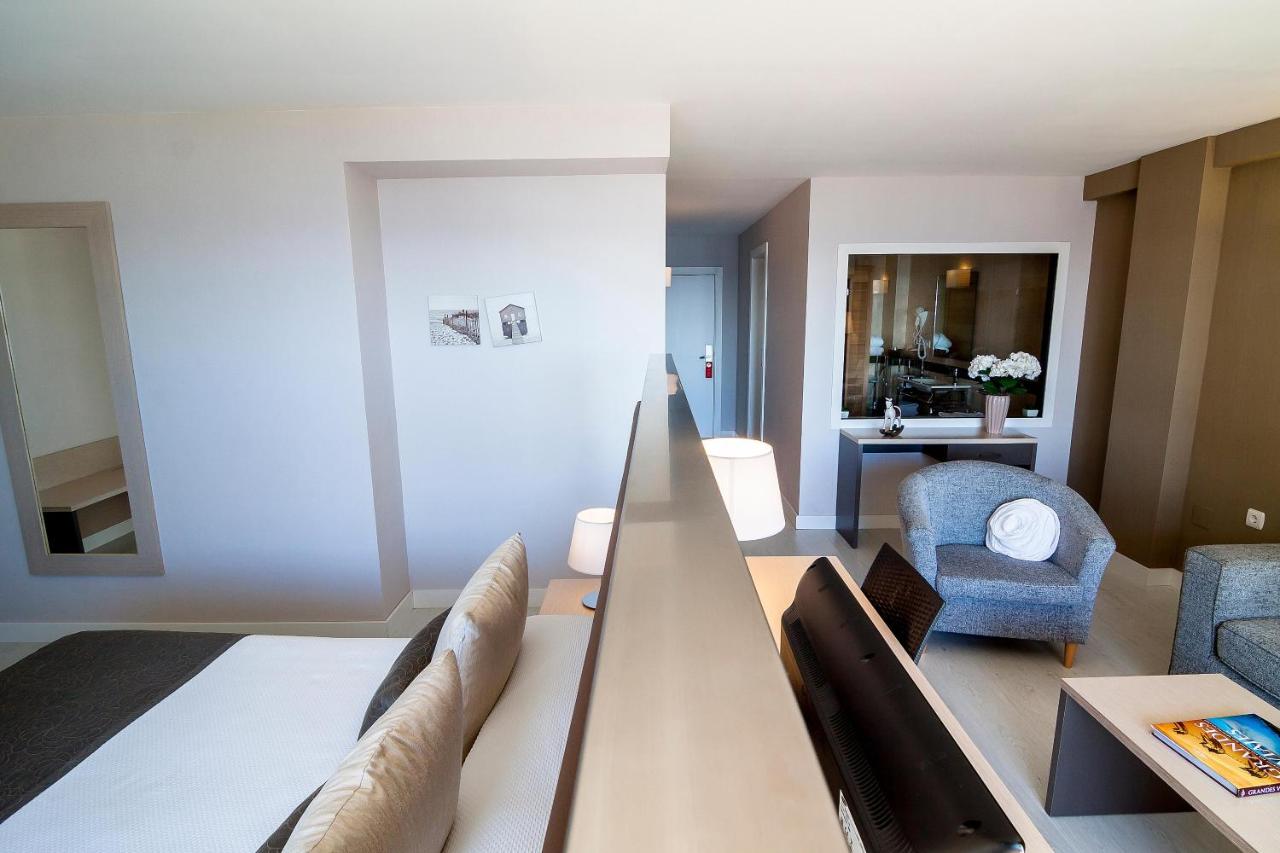 Open-plan room with bed area, lounge chair and interior window to the bathroom.
