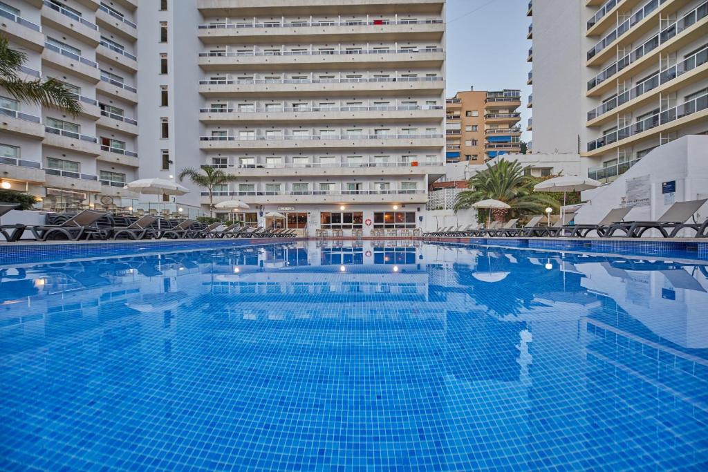 Large outdoor swimming pool with surrounding sun loungers and hotel buildings.