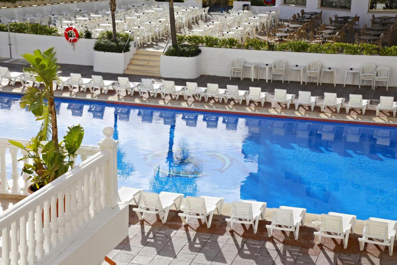Outdoor pool with rows of white loungers and terrace seating above.