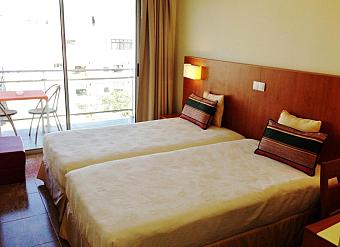 Twin room with balcony seating and daylight through sliding glass doors.