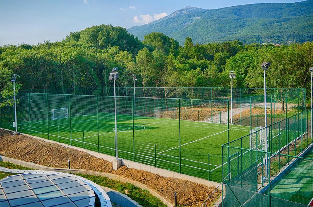 Fenced artificial turf football field with goals and floodlights, used for training camp drills