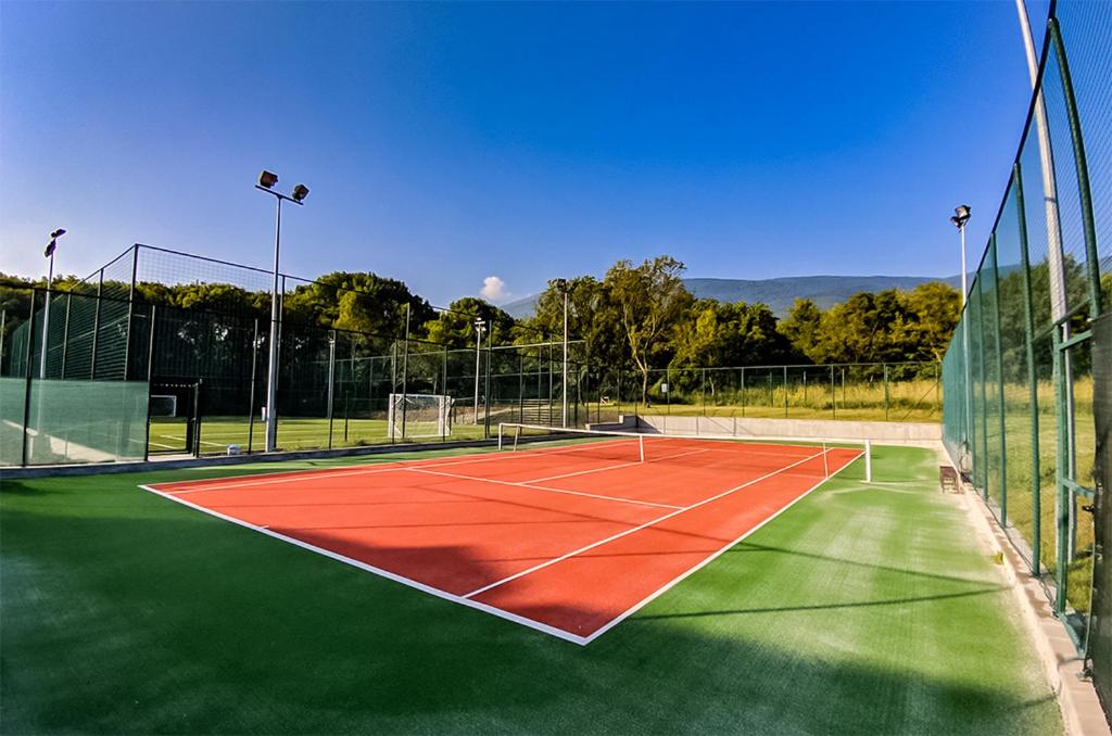 Outdoor tennis court with red and green surface, fenced and lit for training camp practice sessions